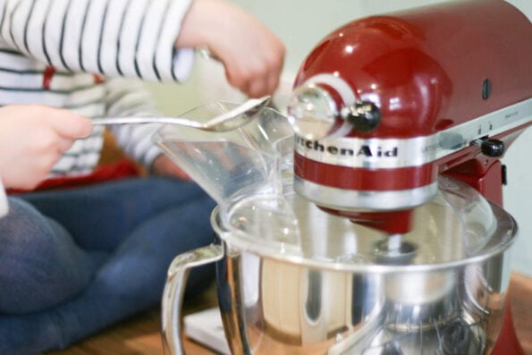 adding sugar to a stand mixer with a small spoon.