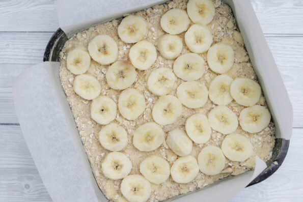 a layer of bananas on top of an oatmeal crumb in a baking tin.