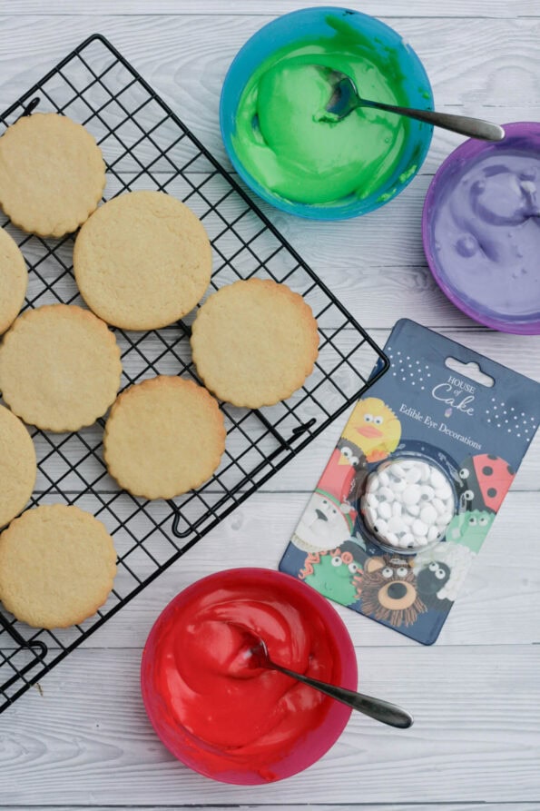 biscuits on a wire rack with coloured icing in small bowls.