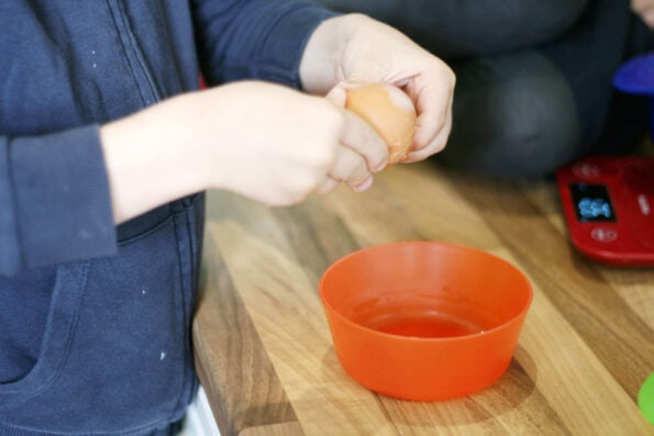 child cracking an egg into a small bowl