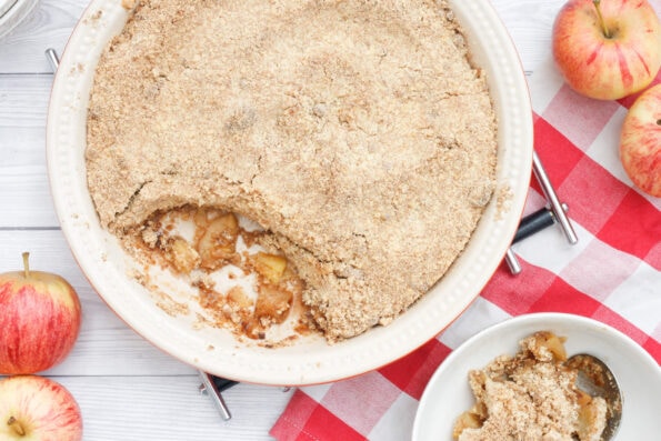Apple crumble in a round baking dish with a portion in a bowl.