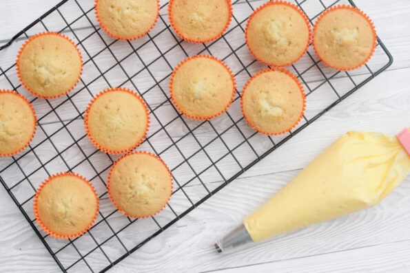 cupcakes on a wire rack with a bag of yellow icing.