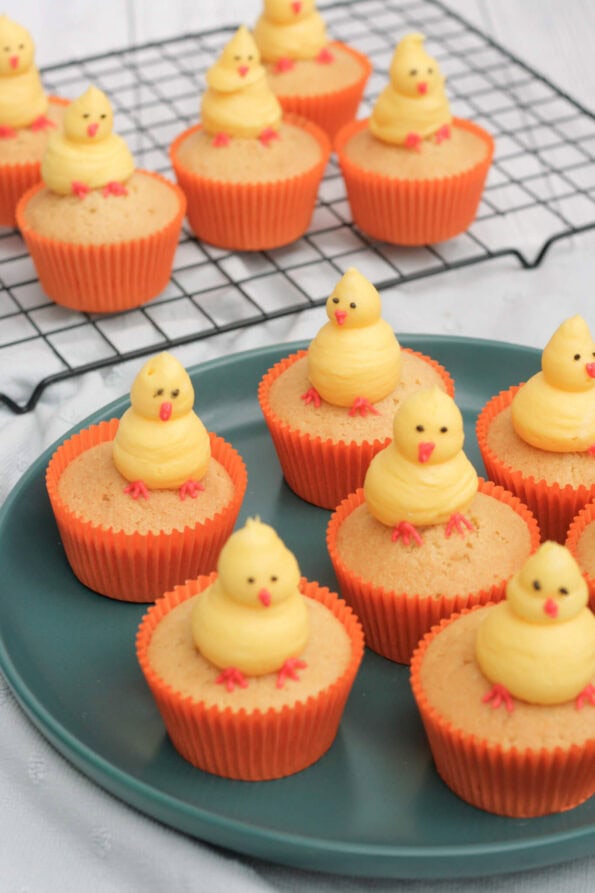 Easter chick cupcakes on a green plate with some on a wire rack in the background.