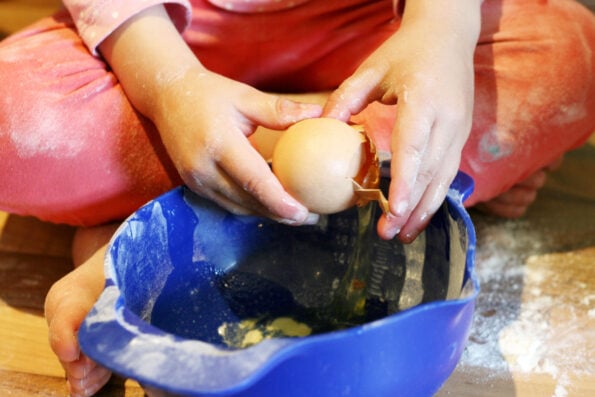 a child cracking an egg into a bowl