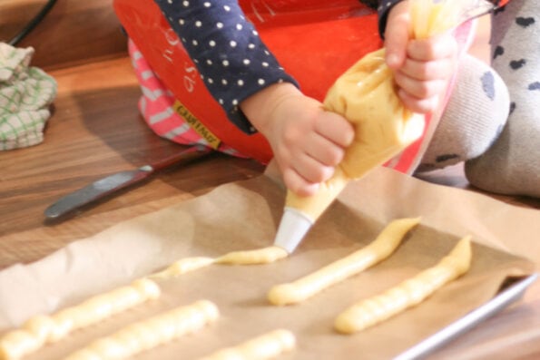 child piping choux pastry into eclairs on a baking tray.