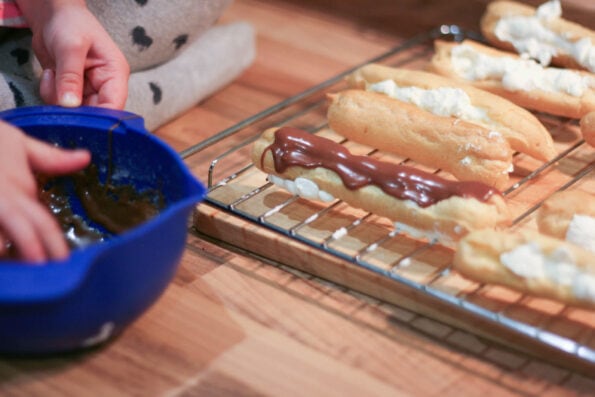 covering chocolate eclairs with chocolate.