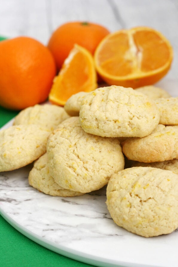 Orange biscuits in a pile with oranges arranged in the background.