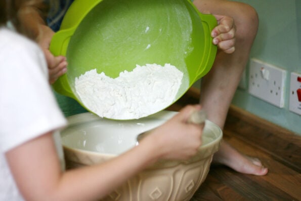 children tipping flour into a bowl.