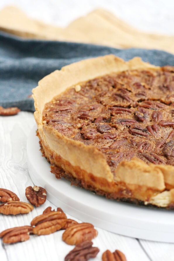 Pecan pie on a serving plate with pecans on the side.