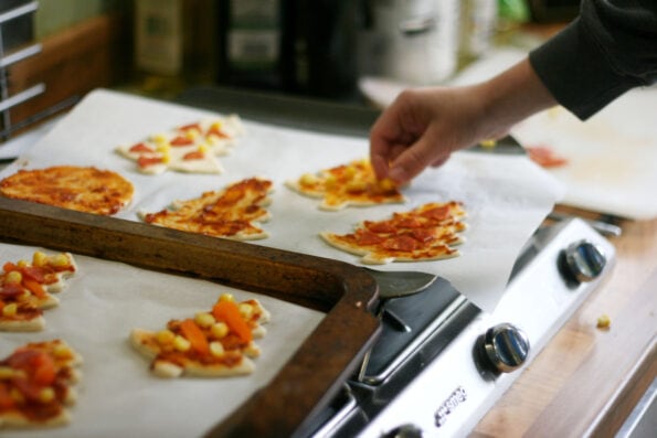Child adding toppings to a christmas tree pizza