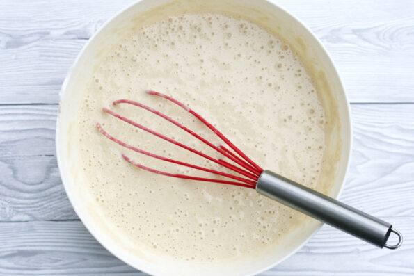 pancake batter in a bowl with a red whisk
