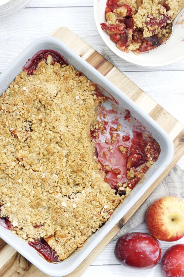 plum and apple crumble in a baking dish with a serving in a bowl