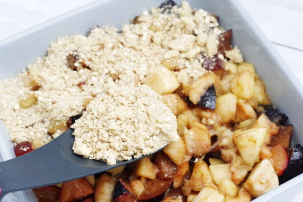 adding crumble topping to plums and apples in a dish
