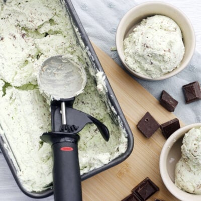mint choc chip ice cream in a dish with a spoon and two bowls of ice cream on the side.