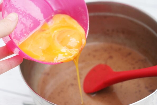 adding egg yolks to chocolate custard in a bowl.
