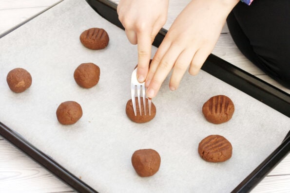 a child pressing a fork into chocolate biscuit dough balls.
