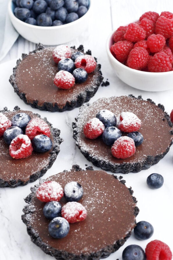 mini no bake chocolate tarts with berries arranged on top.