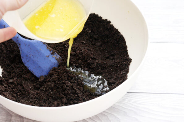 pouring melted butter into a bowl of chocolate biscuit crumbs.