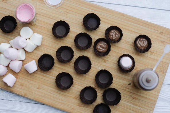 adding marshmallows to petit four cases with melted chocolate in them.