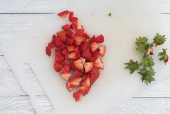 strawberries cut into pieces on a white chopping board.