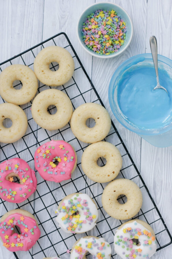 baked doughnuts being glazed on a wire rack.