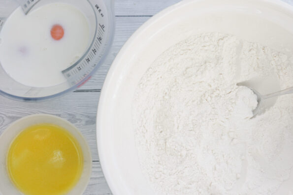 a bowl with melted butter, next to a measuring jug with milk and an egg and a large bowl with flour.