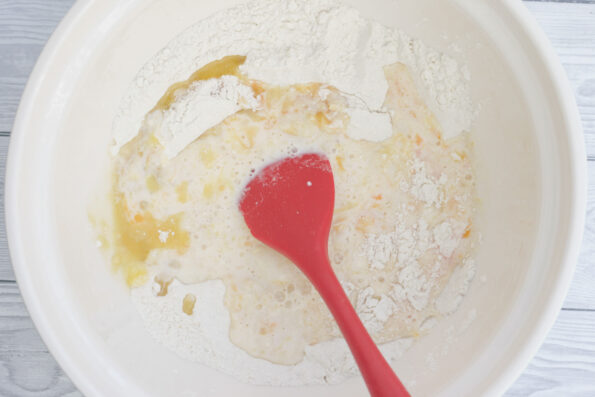 mixing melted butter, egg and milk into a bowl of flour with a red spatula.
