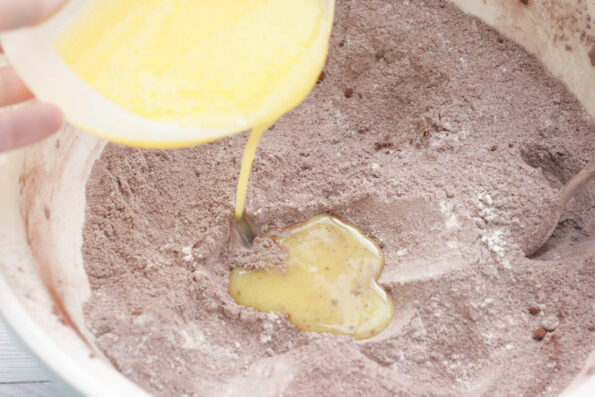 pouring butter into a bowl of flour, cocoa and sugar.